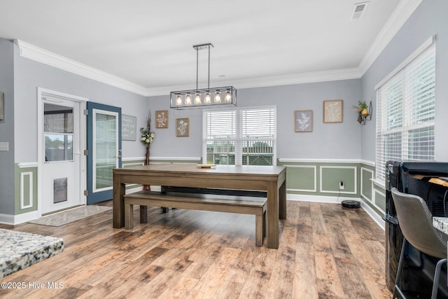 dining room featuring healthy amount of natural light, wood finished floors, ornamental molding, and wainscoting