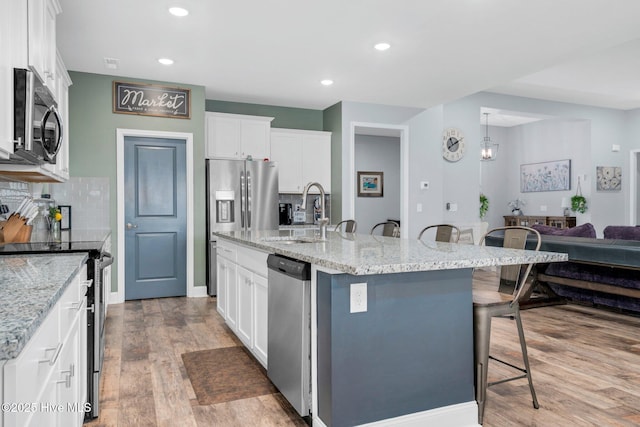 kitchen with stainless steel appliances, a sink, a kitchen bar, light wood-style flooring, and white cabinets