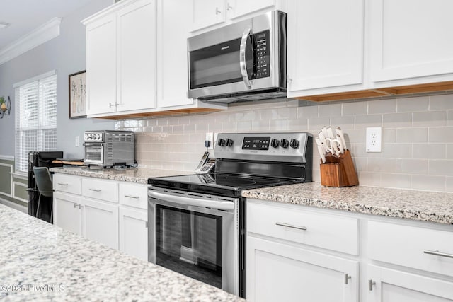 kitchen with appliances with stainless steel finishes, ornamental molding, white cabinetry, tasteful backsplash, and light stone countertops