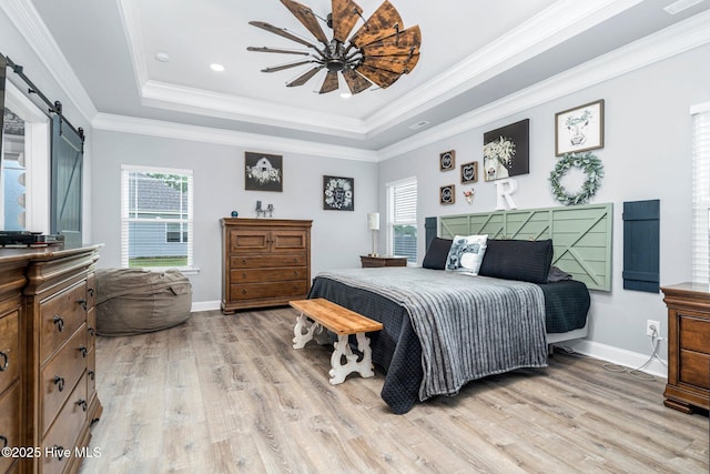bedroom with a barn door, light wood-style flooring, a raised ceiling, multiple windows, and crown molding
