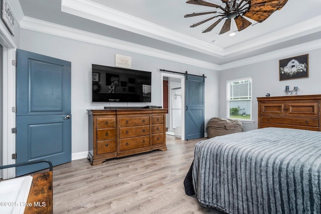 bedroom featuring a raised ceiling, light wood-type flooring, a barn door, ornamental molding, and ceiling fan