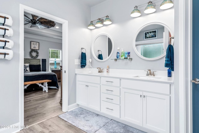 ensuite bathroom featuring double vanity, wood finished floors, baseboards, ornamental molding, and a ceiling fan