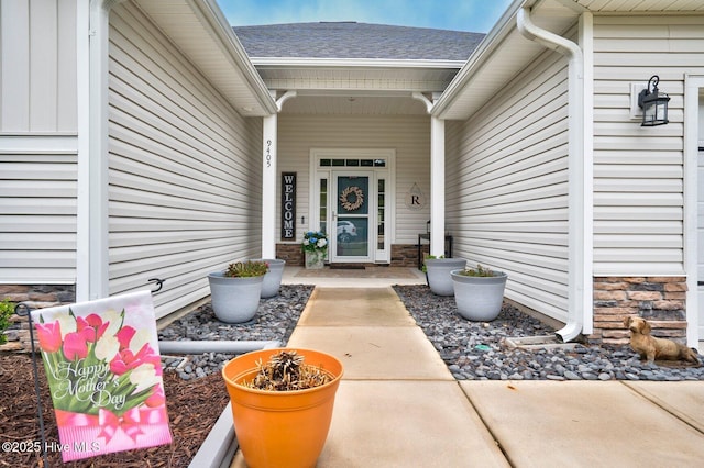entrance to property with stone siding and roof with shingles