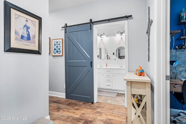 corridor featuring a barn door, a sink, light wood finished floors, and baseboards