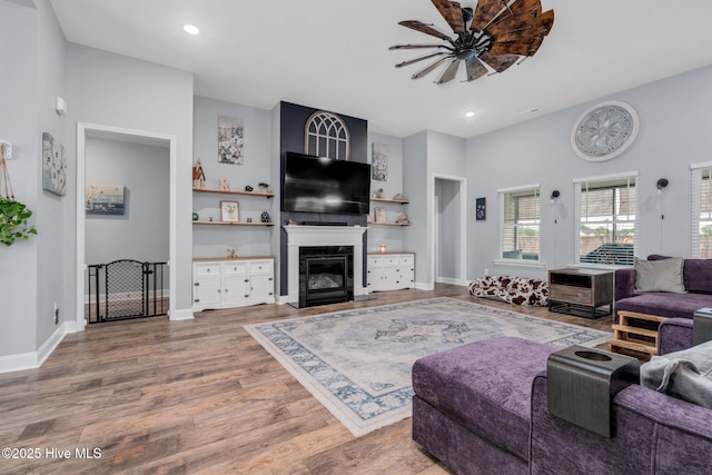 living room with a ceiling fan, a glass covered fireplace, wood finished floors, baseboards, and recessed lighting