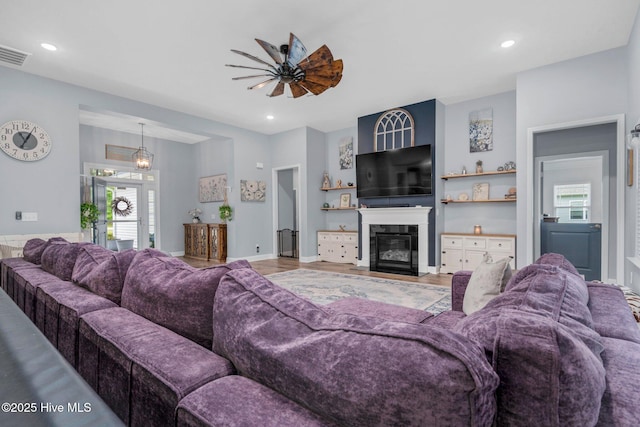 living area featuring a glass covered fireplace, ceiling fan, recessed lighting, and wood finished floors