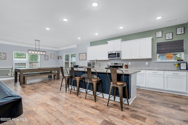 kitchen featuring stainless steel appliances, ornamental molding, white cabinets, light wood-style flooring, and a kitchen island with sink