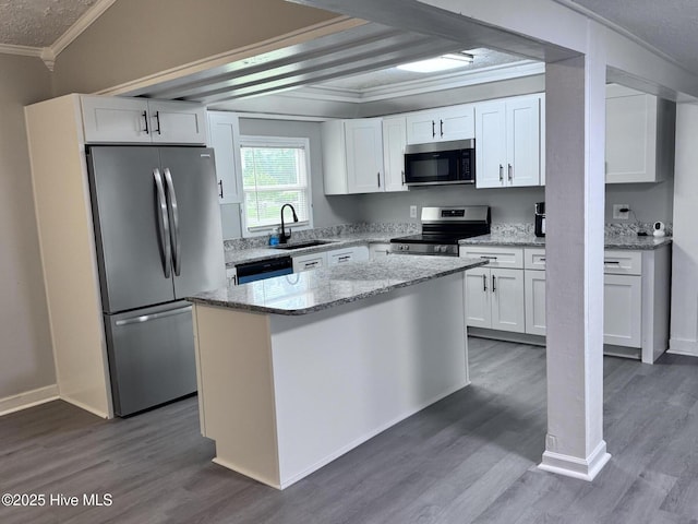 kitchen featuring appliances with stainless steel finishes, ornamental molding, a sink, white cabinetry, and wood finished floors