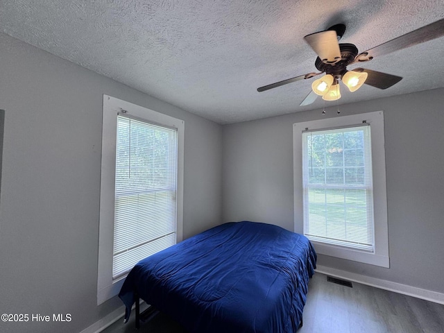 bedroom with wood finished floors, baseboards, a textured ceiling, and ceiling fan