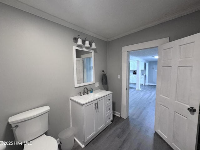 half bathroom featuring toilet, ornamental molding, wood finished floors, vanity, and baseboards