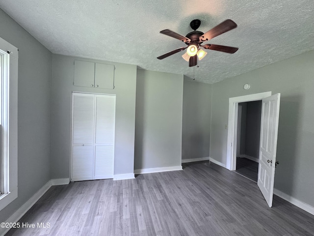 unfurnished bedroom featuring a textured ceiling, wood finished floors, baseboards, a closet, and a ceiling fan