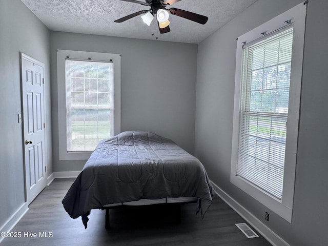 bedroom featuring multiple windows, a textured ceiling, wood finished floors, and baseboards
