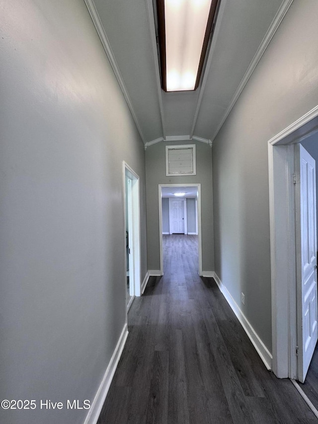 hallway featuring dark wood-type flooring, vaulted ceiling, ornamental molding, and baseboards