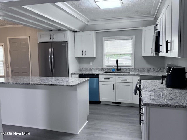 kitchen featuring freestanding refrigerator, stainless steel microwave, a sink, dishwashing machine, and white cabinetry