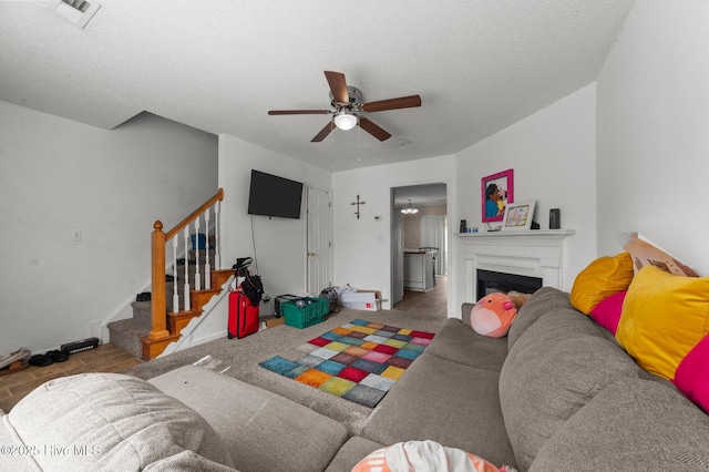 living room featuring ceiling fan, stairway, a textured ceiling, baseboards, and a fireplace
