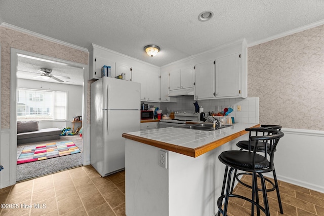 kitchen with freestanding refrigerator, a textured ceiling, under cabinet range hood, range with electric stovetop, and a peninsula