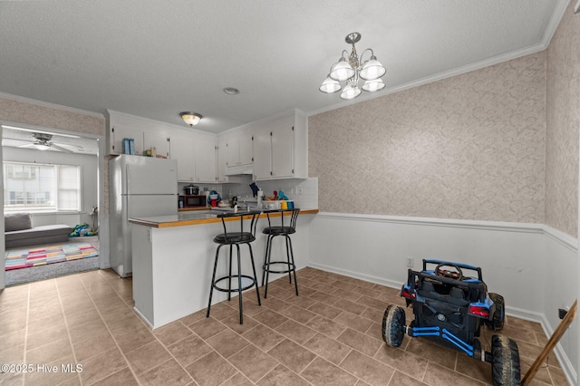 kitchen featuring freestanding refrigerator, crown molding, a textured ceiling, under cabinet range hood, and white cabinets