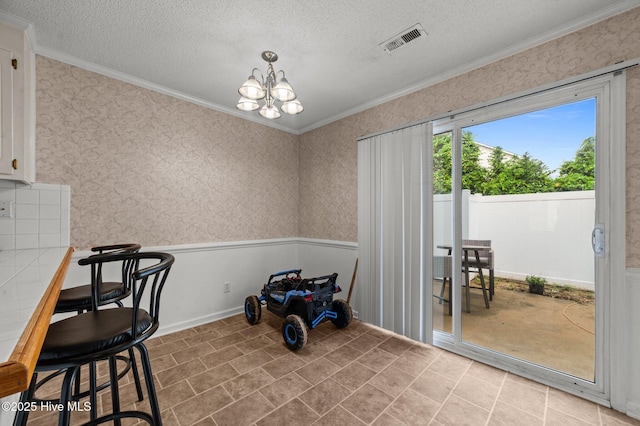 unfurnished dining area featuring ornamental molding, a chandelier, a textured ceiling, wallpapered walls, and light tile patterned flooring