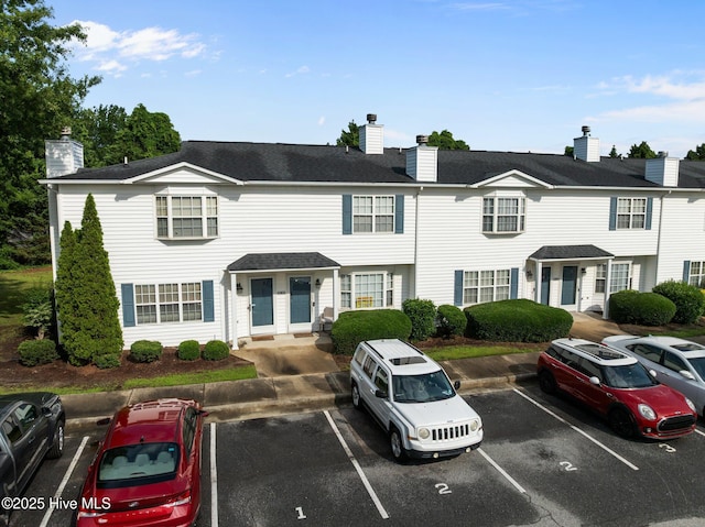 view of property featuring a chimney, uncovered parking, and a shingled roof
