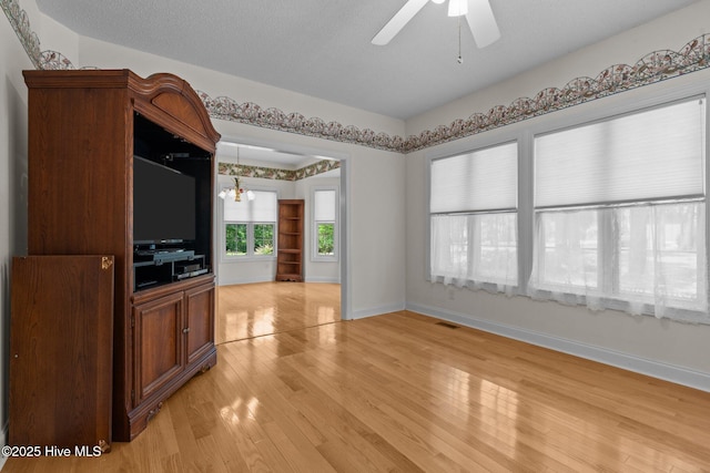 unfurnished living room with light wood-style floors, ceiling fan, baseboards, and a chandelier