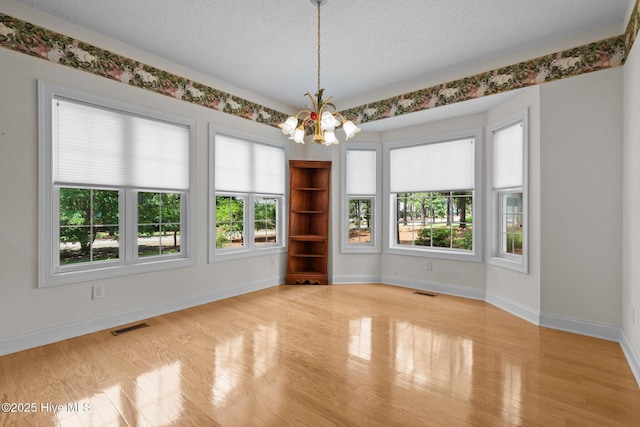 spare room with a chandelier, wood finished floors, baseboards, and a textured ceiling