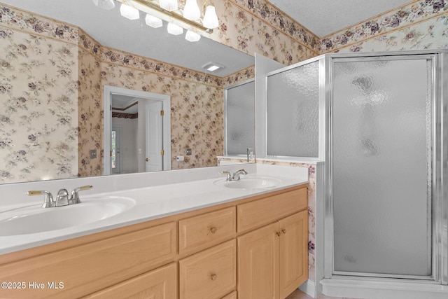 bathroom with wallpapered walls, a shower stall, and double vanity
