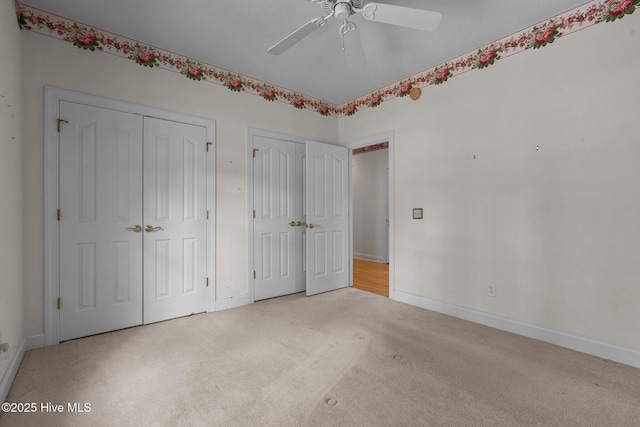 unfurnished bedroom featuring two closets, carpet flooring, baseboards, and ceiling fan