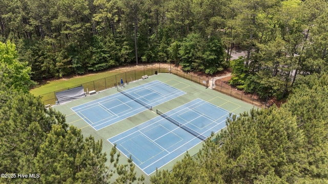 view of tennis court featuring fence and a forest view