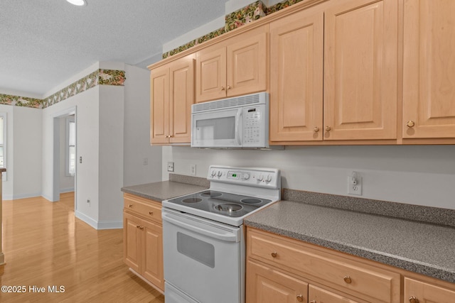 kitchen featuring white appliances, dark countertops, light brown cabinetry, a textured ceiling, and light wood finished floors