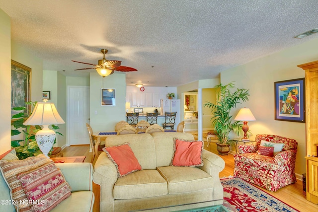 living room featuring light wood-style floors, ceiling fan, a textured ceiling, and baseboards