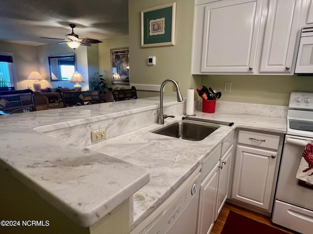 kitchen featuring white appliances, a sink, open floor plan, a peninsula, and white cabinets