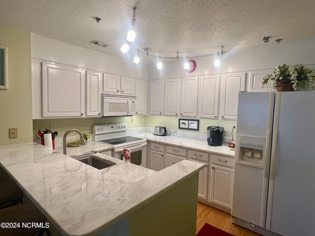 kitchen with white appliances, a sink, a peninsula, track lighting, and white cabinetry