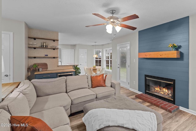 living area with a fireplace, wood finished floors, ceiling fan, and baseboards