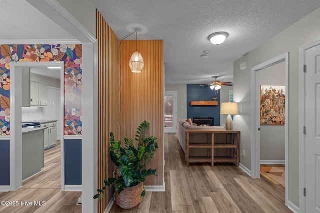 hall with a textured ceiling, light wood-type flooring, and baseboards