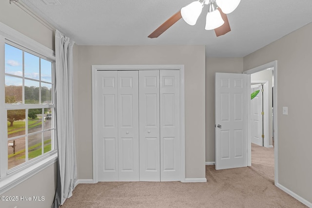 unfurnished bedroom featuring light colored carpet, a closet, baseboards, and ceiling fan