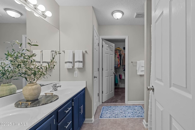 bathroom with a textured ceiling, double vanity, a spacious closet, and baseboards