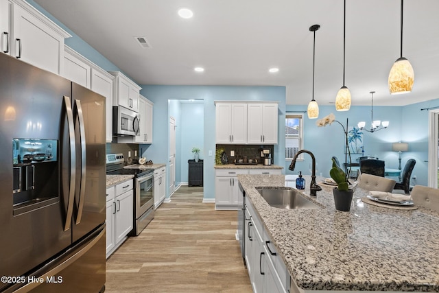 84 Capital Dr, Hampstead, NC 28443 - kitchen with stainless steel appliances, a sink, light wood finished floors, white cabinets, and tasteful backsplash
