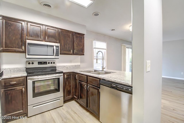 kitchen featuring appliances with stainless steel finishes, a sink, light wood finished floors, and dark brown cabinets
