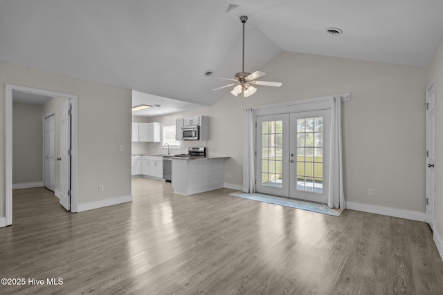 120 NW 19th St, Oak Island, NC 28465 - unfurnished living room with french doors, a ceiling fan, light wood-style flooring, baseboards, and high vaulted ceiling