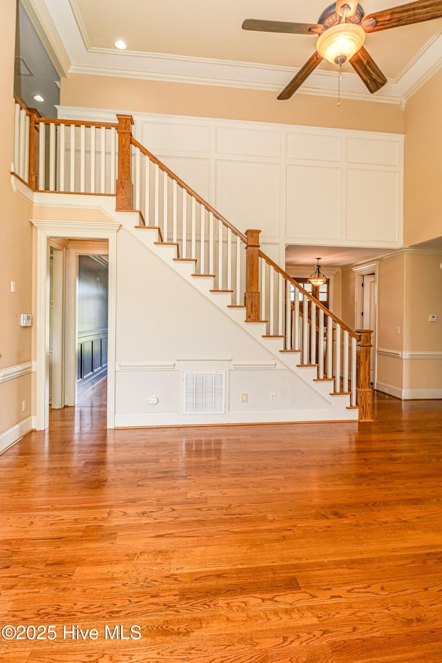 unfurnished living room with ornamental molding, stairway, light wood finished floors, ceiling fan, and a towering ceiling