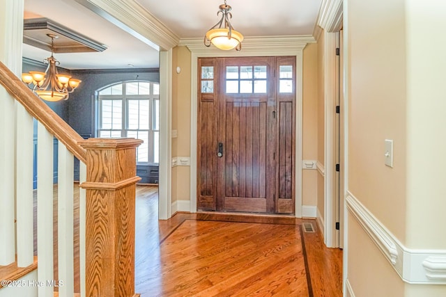 entrance foyer with wood finished floors, ornamental molding, a chandelier, stairs, and baseboards