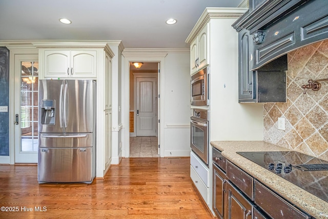 kitchen with stainless steel appliances, backsplash, light stone counters, light wood finished floors, and cream cabinetry