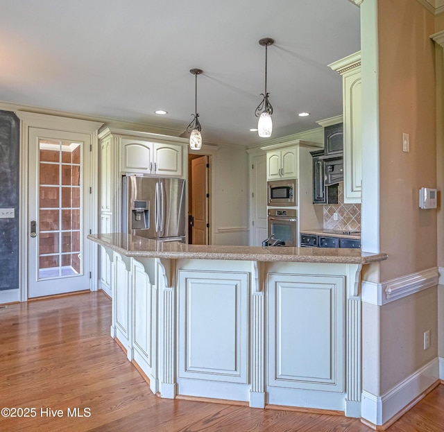 kitchen with appliances with stainless steel finishes, a peninsula, tasteful backsplash, a kitchen breakfast bar, and baseboards
