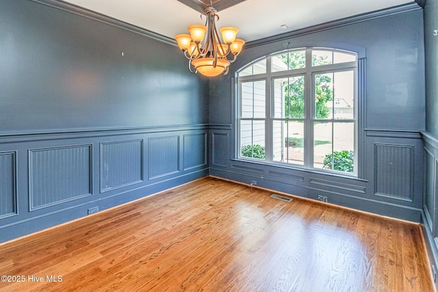 spare room with a decorative wall, healthy amount of natural light, a chandelier, wood finished floors, and crown molding