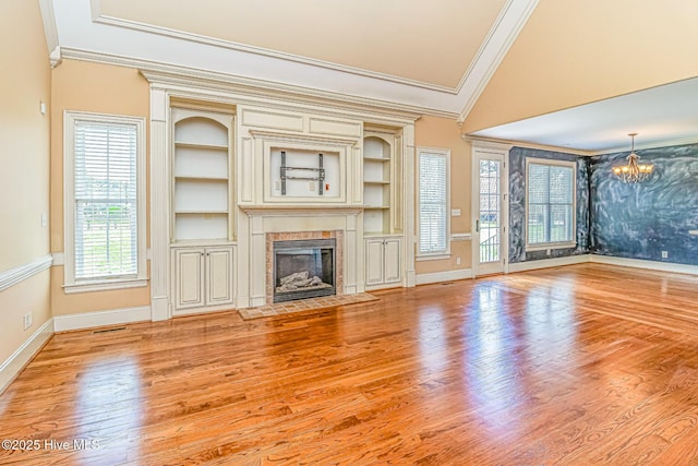 unfurnished living room featuring ornamental molding, a chandelier, a tile fireplace, baseboards, and wood finished floors