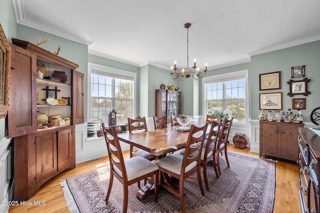 208 Sea Manor Dr, Surf City, NC 28445 - dining area featuring healthy amount of natural light, a chandelier, light wood-type flooring, crown molding, and a wainscoted wall