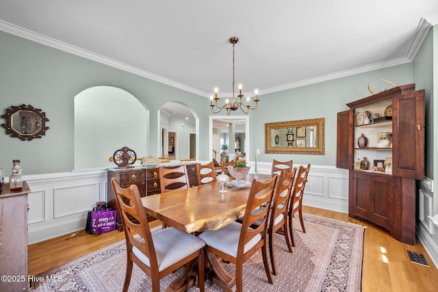 208 Sea Manor Dr, Surf City, NC 28445 - dining room featuring light wood finished floors, arched walkways, crown molding, a wainscoted wall, and a chandelier