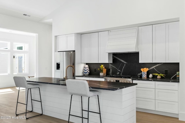 609 Augusta Ave, Carolina Beach, NC 28428 - kitchen featuring custom range hood, stainless steel fridge, dark countertops, backsplash, and white cabinetry