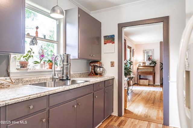 kitchen with a sink, gray cabinets, crown molding, light wood-style floors, and hanging light fixtures