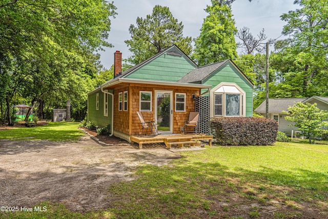 view of front of property featuring a chimney, a front yard, a deck, and a shingled roof